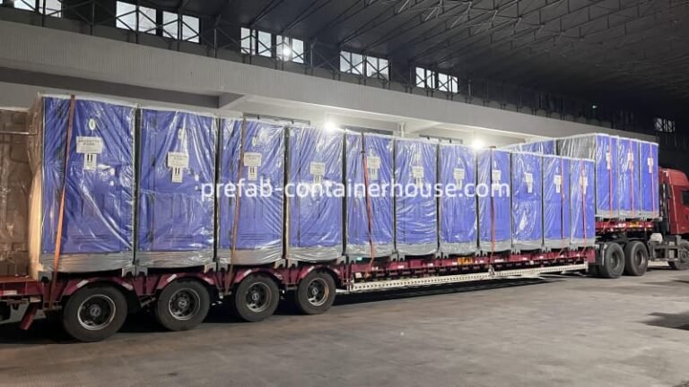 A long flatbed truck loaded with a row of blue portable toilets wrapped in protective plastic film for shipping.